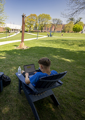 decorative - male student sitting in adirondack chair on the lawn